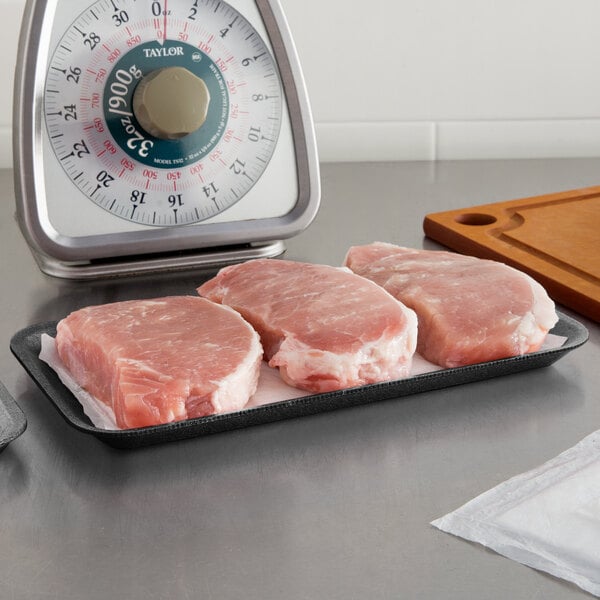 A black CKF foam meat tray with raw meat on a counter.