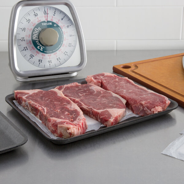 A piece of raw meat on a CKF black foam meat tray on a counter next to a scale.