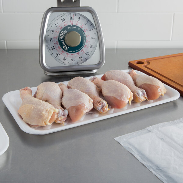 A white CKF foam tray holding raw chicken legs on a counter.