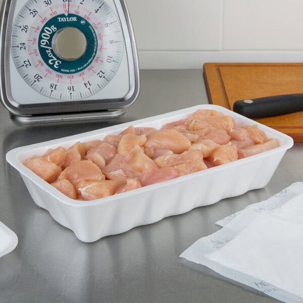A white CKF foam meat tray holding raw chicken meat on a counter.