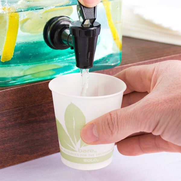 A hand pouring water from a faucet into a Bare by Solo paper cold cup.