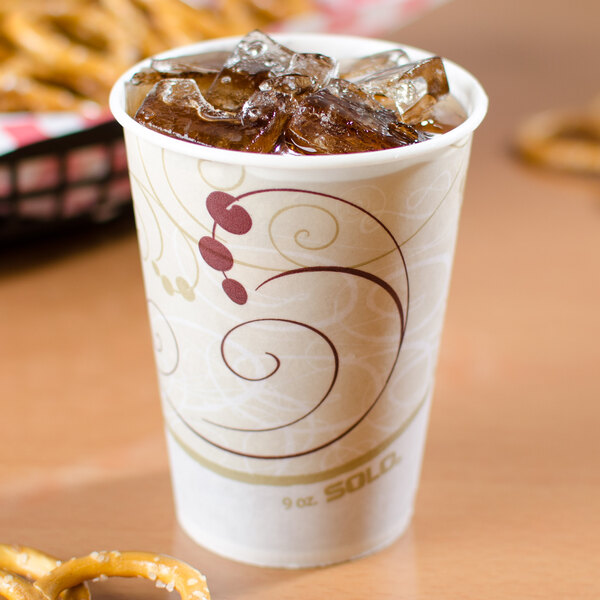 A Solo wax treated paper cold cup with ice and a drink on a table with pretzels.