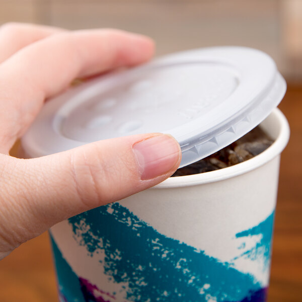 A hand placing a Solo translucent plastic lid on a cold cup with a blue straw slot and identification buttons.