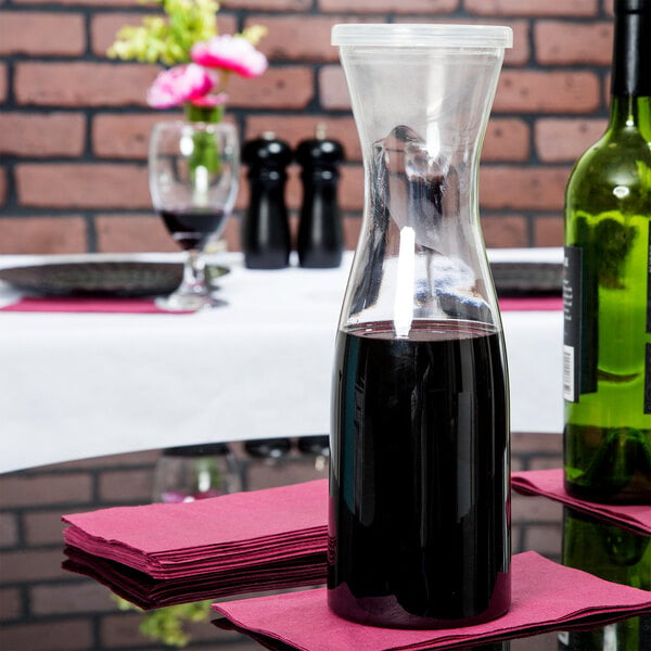 A clear plastic carafe with a dark liquid in it on a table with a white tablecloth.