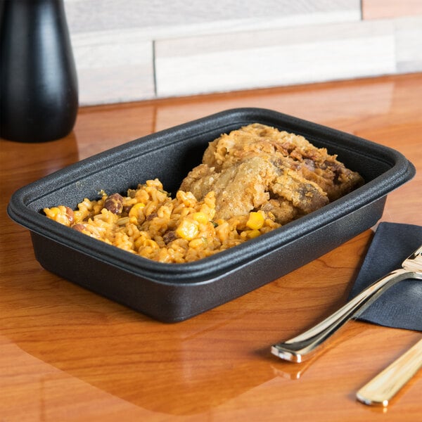 A black Genpak rectangular microwaveable container with food in it sitting on a table.