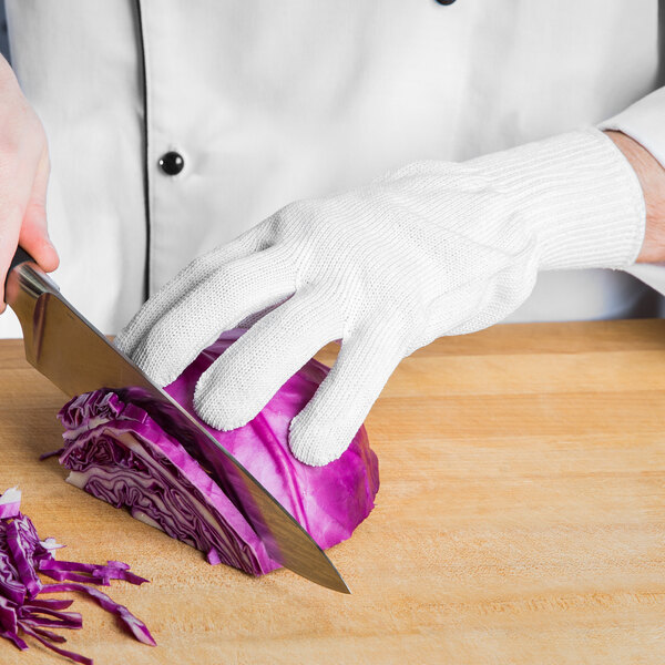 A person's hand in a San Jamar white glove cutting a piece of cabbage.