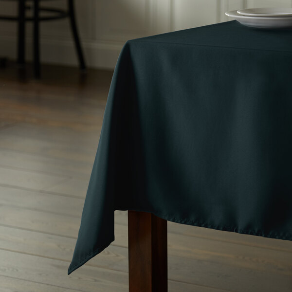 A rectangular table with a hunter green Intedge cloth and a white plate on it.