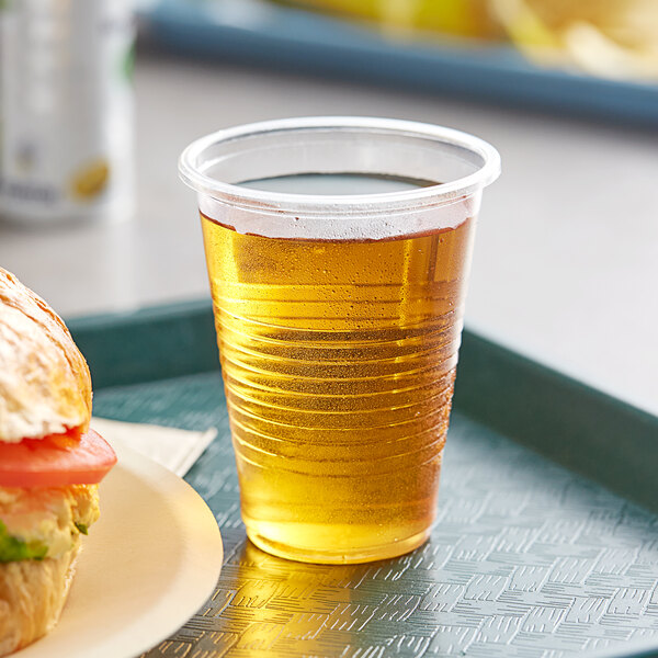 A Choice translucent plastic cup with a drink in it next to a sandwich on a tray.