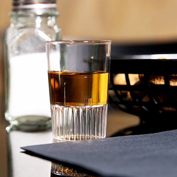 A Fineline clear hard plastic shooter glass filled with brown liquid on a table in a bar.