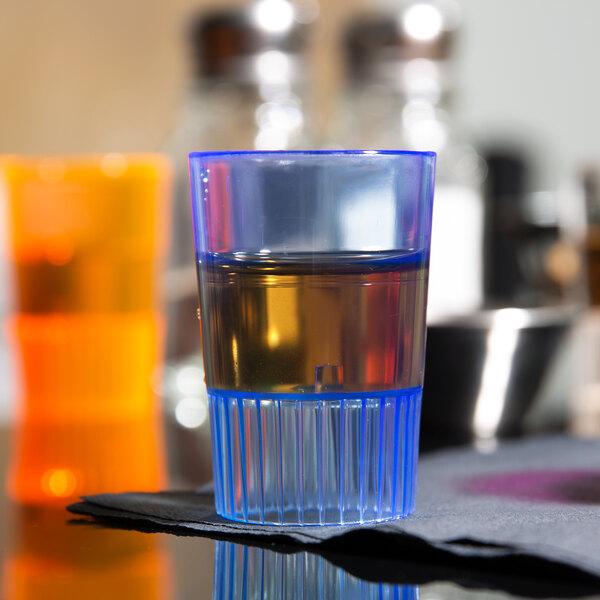 A close-up of a Fineline blue plastic shooter glass filled with brown liquid.
