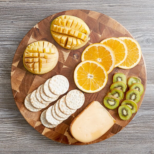 A Tablecraft Acacia Wood end grain chopping board with cut up fruit and cheese on a wood surface.