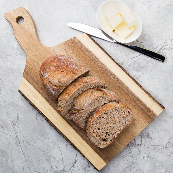 A Tablecraft acacia wood serving board with sliced bread and butter on a table.