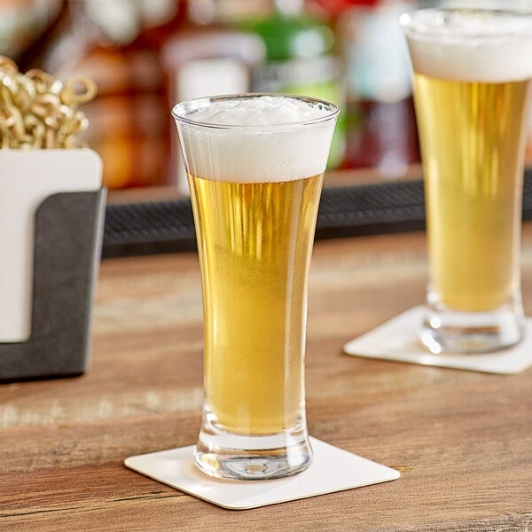 Two Acopa flared pilsner glasses filled with beer on a wooden table.