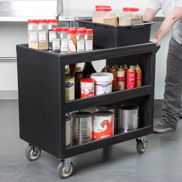 A black Cambro three shelf service cart with food containers and cans on it.
