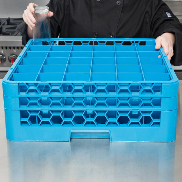A chef holding a blue plastic Carlisle glass rack with extenders.