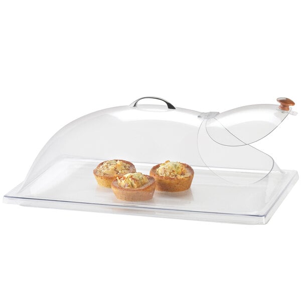 A Cal-Mil clear plastic dome cover with a single end opening on a glass tray with muffins inside.