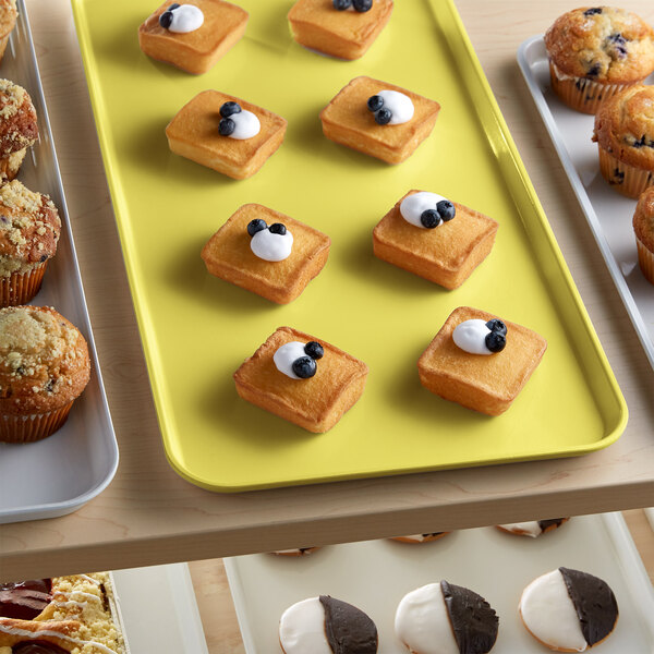 A yellow Cambro market tray holding square bread and pastries with white and blueberry toppings.