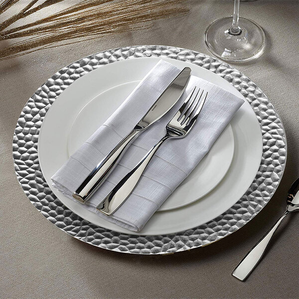 A white plastic charger plate with silverware on it.