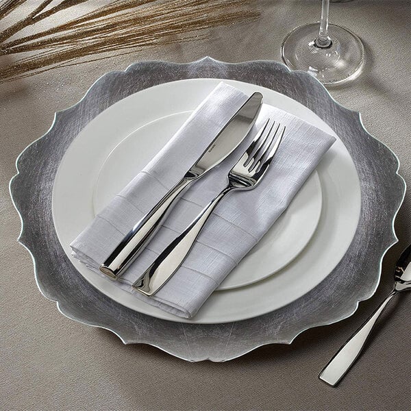 A silver plastic charger with silverware on a plate.