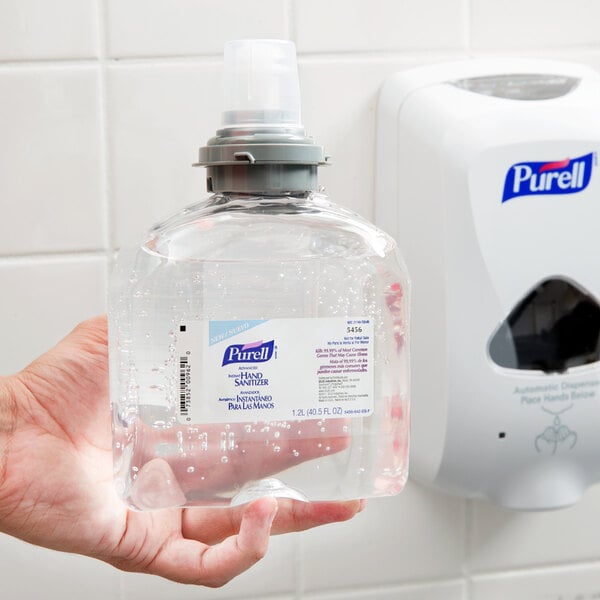 A hand holding a Purell TFX Advanced hand sanitizer bottle.