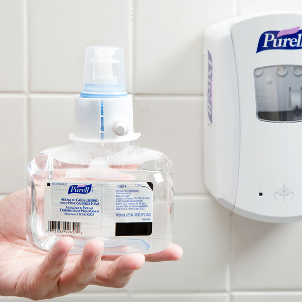 A hand holding a plastic bottle of Purell foaming hand sanitizer.