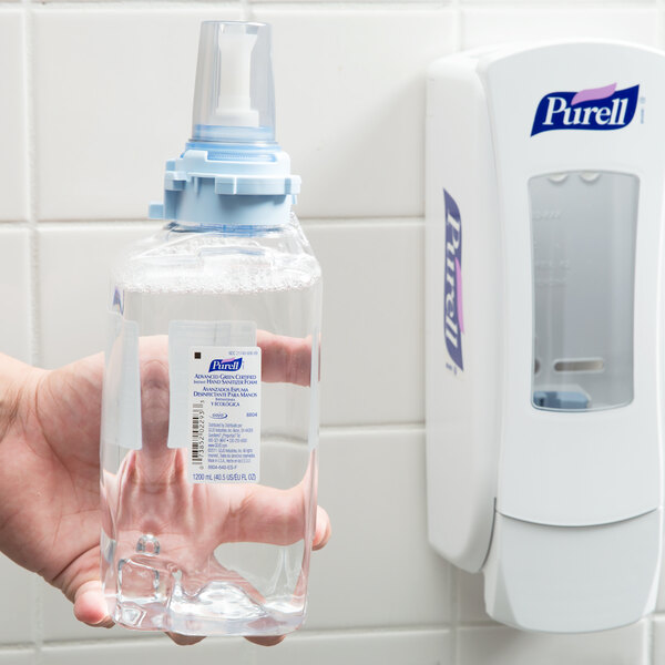 A hand holding a plastic bottle of Purell foaming hand sanitizer.