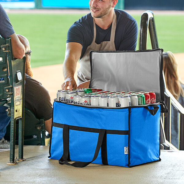 A man in an apron holding a Choice blue large insulated cooler bag filled with cans of beer.