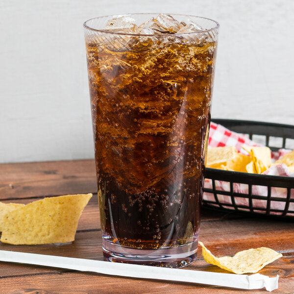 A clear customizable plastic tumbler filled with soda and ice on a table with chips.
