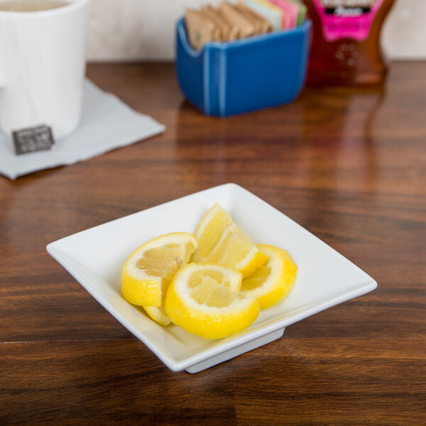 A Bright White Square Porcelain bowl filled with lemon slices on a table.