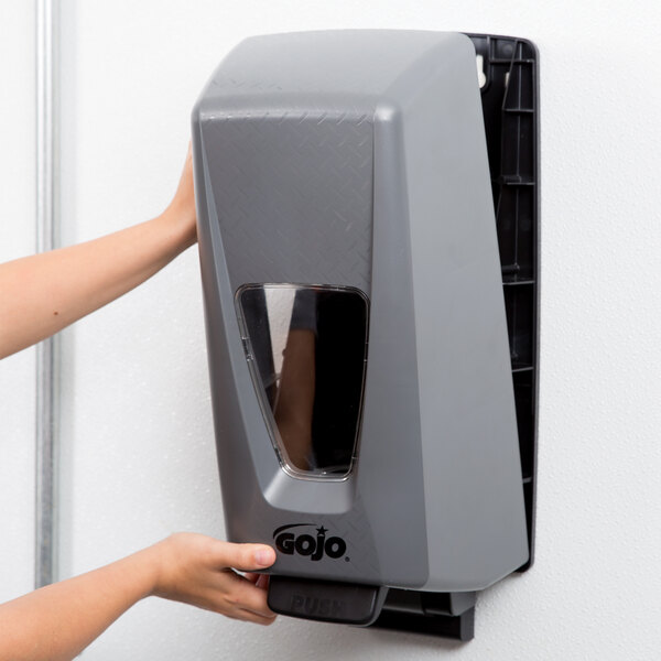 A person's hand using a GOJO gray hand sanitizer dispenser.