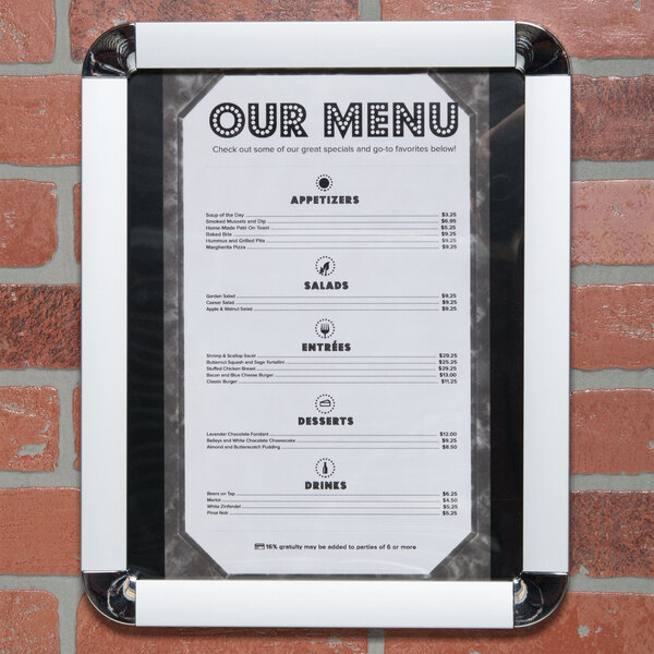 A white menu board in a satin aluminum frame with round corners on a brick wall.