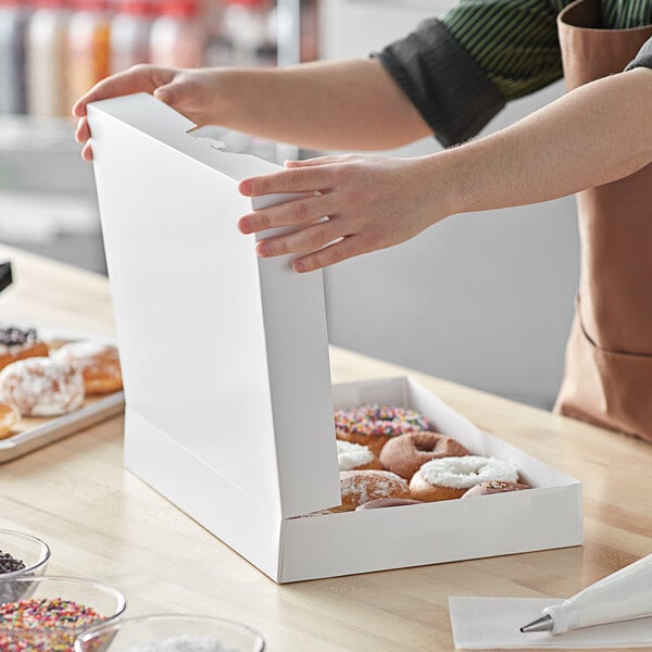 A person opening a white Baker's Mark box of doughnuts on a counter.