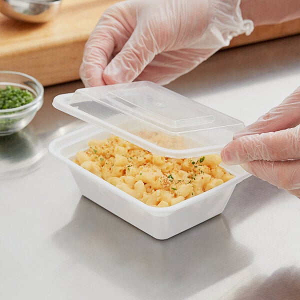 A gloved hand fills a Choice white rectangular plastic container with macaroni and cheese.