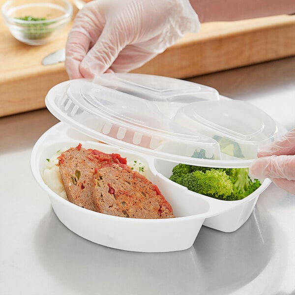 A gloved hand holding a Choice white plastic container with compartments filled with food.