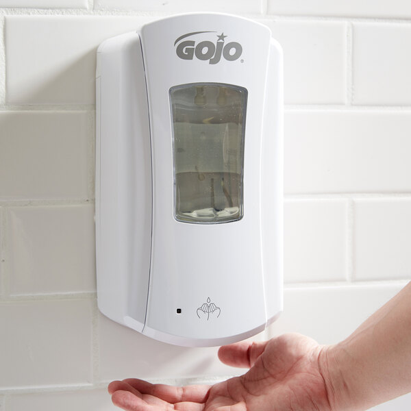 A person's hand using a white GOJO touchless soap dispenser.