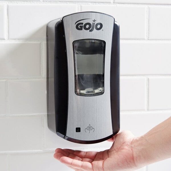 A hand using a GOJO chrome touchless hand soap dispenser.