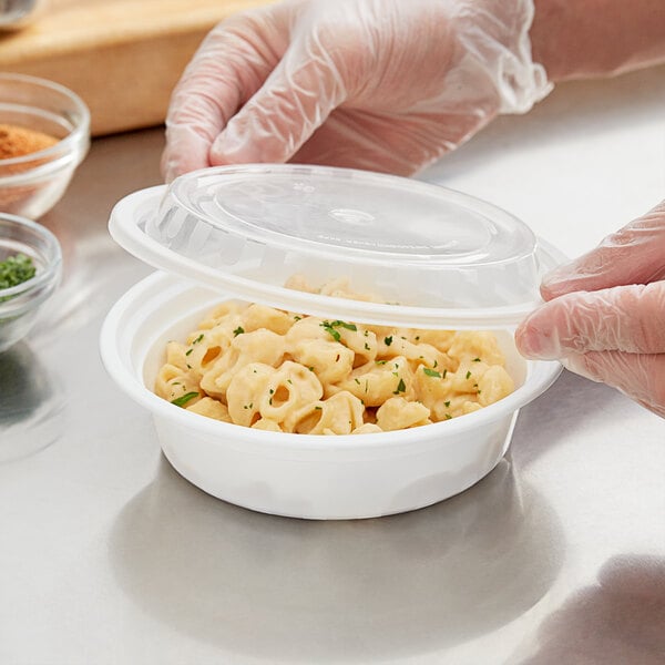 A person in gloves putting pasta in a Choice white plastic microwaveable container.