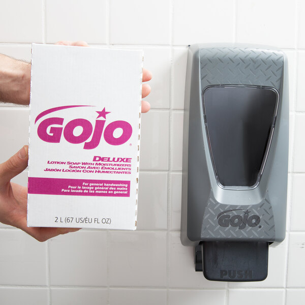 A hand holding a white box of GOJO Deluxe Floral Lotion Hand Soap with pink text.