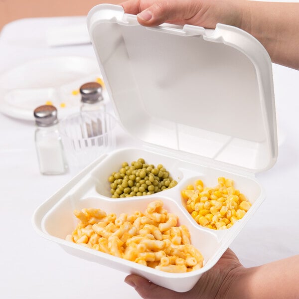 A hand holding a white Genpak foam container with 3 compartments of food.