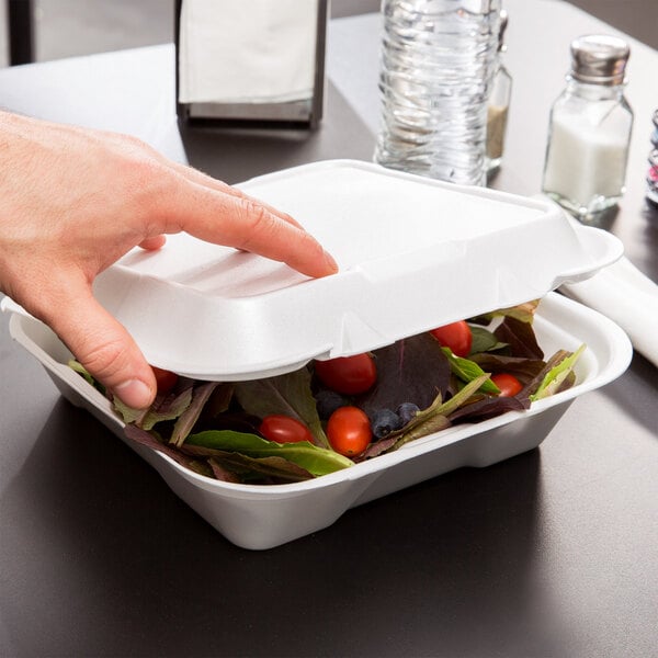 A hand reaching out to take out a salad from a white Genpak foam container.