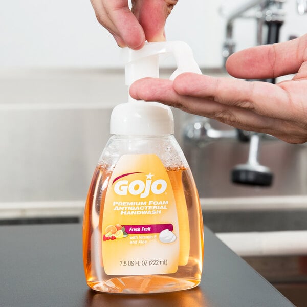 A person using a GOJO Fresh Fruit foaming hand soap dispenser on a counter.