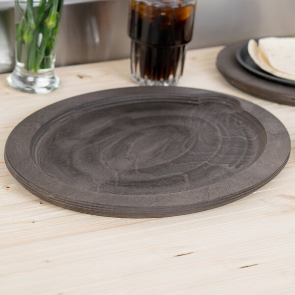 A Lodge oval wooden underliner with a plate and a drink on a table.