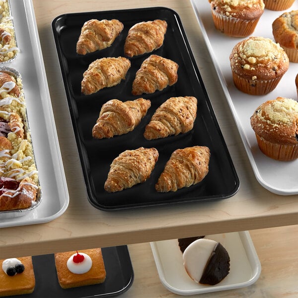 A black Cambro market tray filled with pastries and muffins on a bakery display counter.