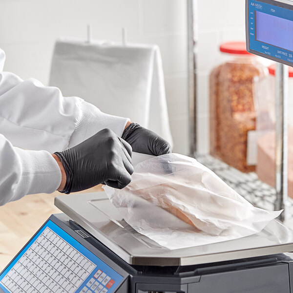 A person in a white lab coat and black gloves weighing food on a Choice Deli Saddle Bag Stand.