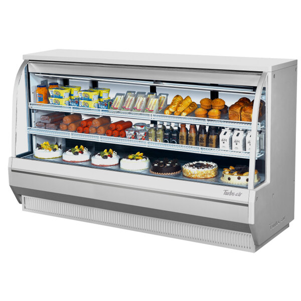 A Turbo Air white curved glass refrigerated deli case with food on shelves.
