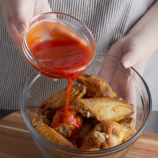 A person pouring Crystal hot sauce onto a bowl of chicken wings.