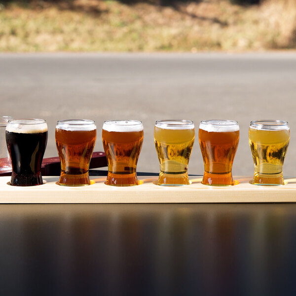 A row of Libbey Mini Pub Tasting Glasses on a natural flight paddle filled with dark liquid.