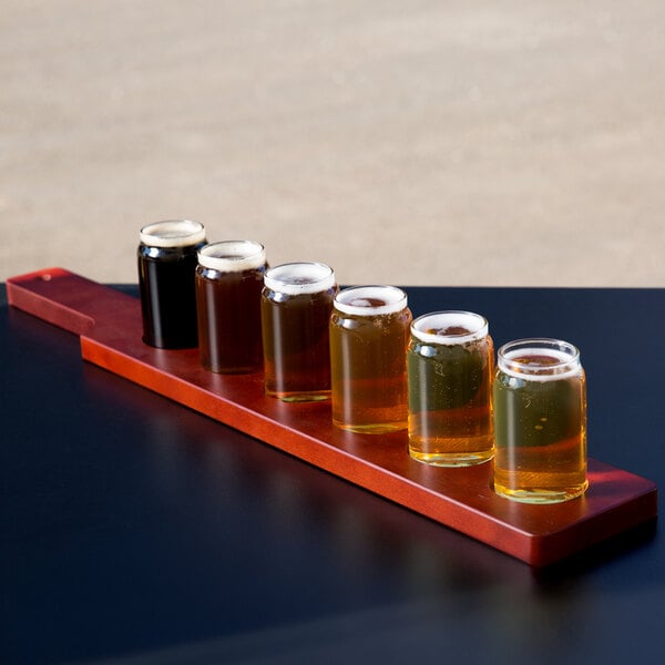 A row of Libbey Mini Can Tasting Glasses filled with beer on a mahogany flight paddle.