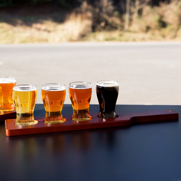 A row of Libbey Mini Pub Tasting Glasses on a Mahogany Flight Paddle filled with beer.