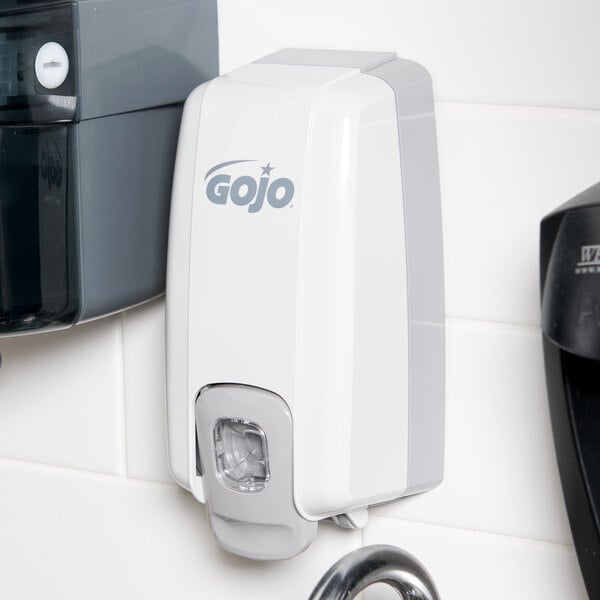 A white and grey GOJO NXT manual hand soap dispenser with a logo on it.